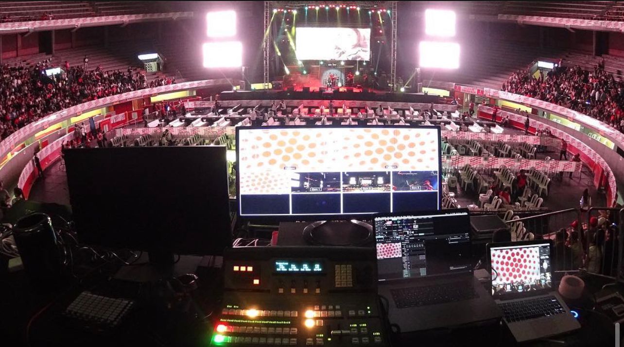 Live event screens and a concert stage viewed from the production control desk in an arena