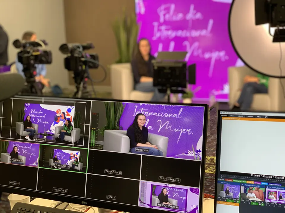 A broadcast monitor showing multiple camera views of a speaker in a purple studio set