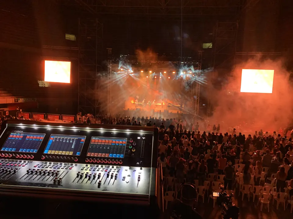 A packed concert audience and orange stage lighting viewed from the mixing desk