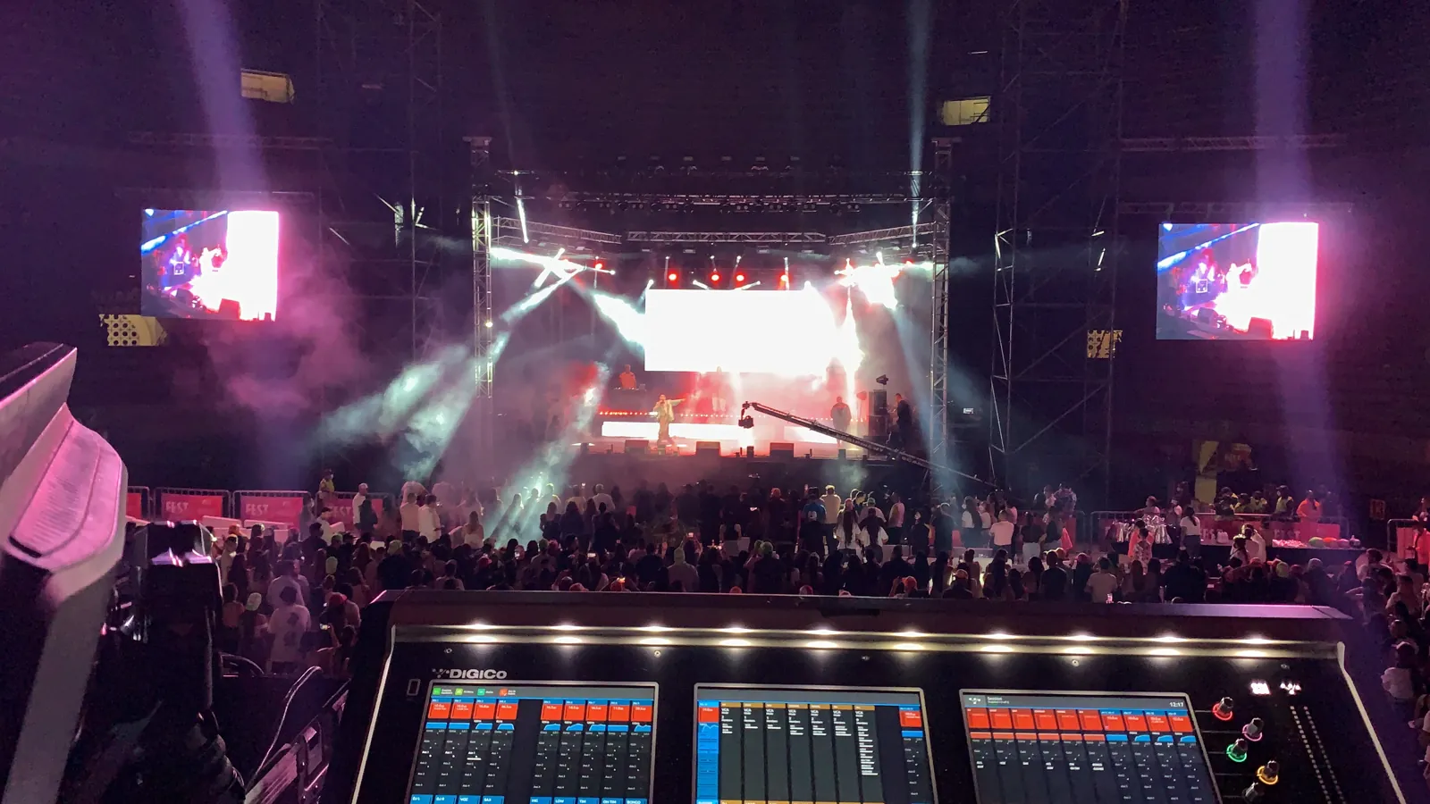 A live concert seen from the production desk, with a full audience and dramatic stage lighting