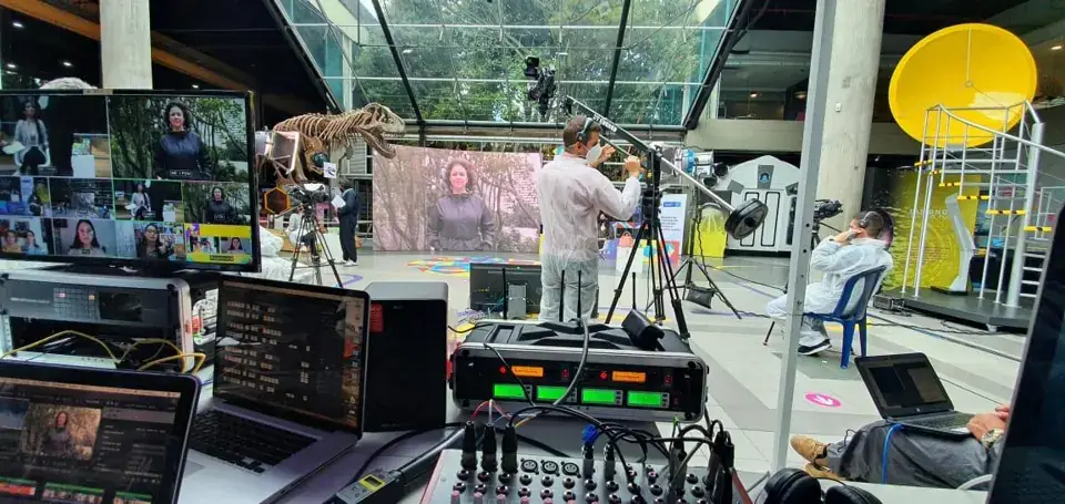 Cameras, laptops, and a production desk overlooking a stage in a glass-roofed venue