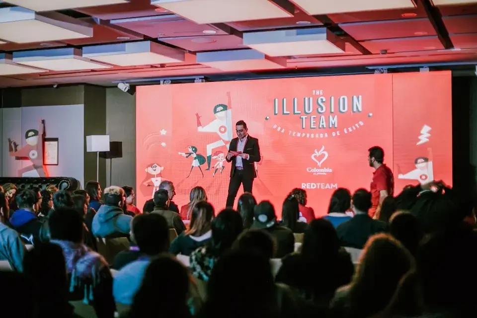 A presenter speaking to an audience in front of a red event backdrop