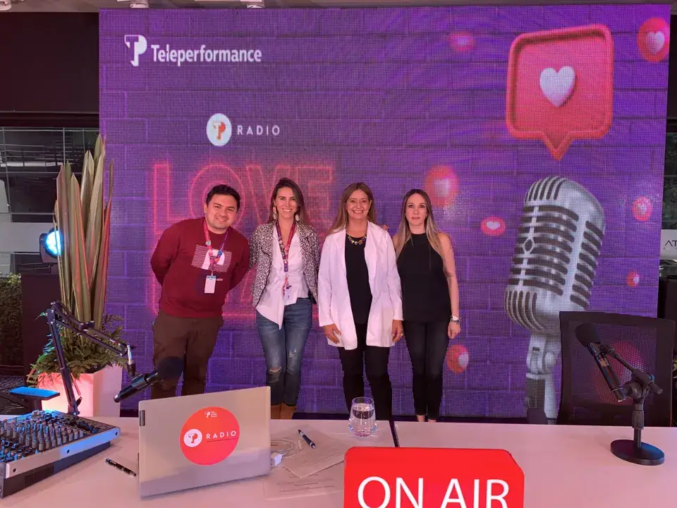 Four presenters together behind an on-air sign in a colorful studio